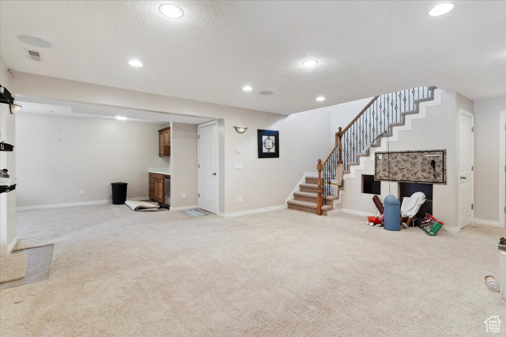 Finished below grade area with light carpet, stairway, baseboards, recessed lighting, and a textured ceiling