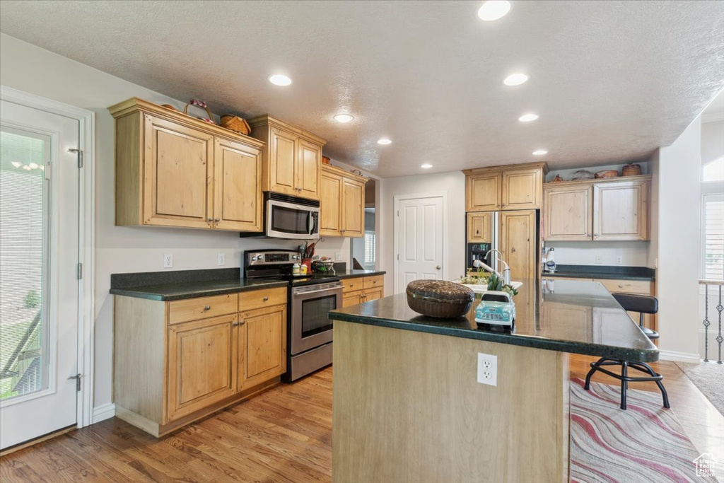 Kitchen featuring stainless steel appliances, dark countertops, a kitchen breakfast bar, baseboards, and light wood finished floors