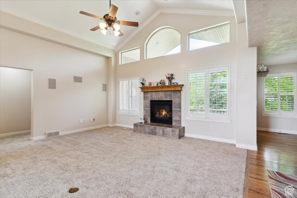 Unfurnished living room with a ceiling fan, a tile fireplace, crown molding, baseboards, and high vaulted ceiling
