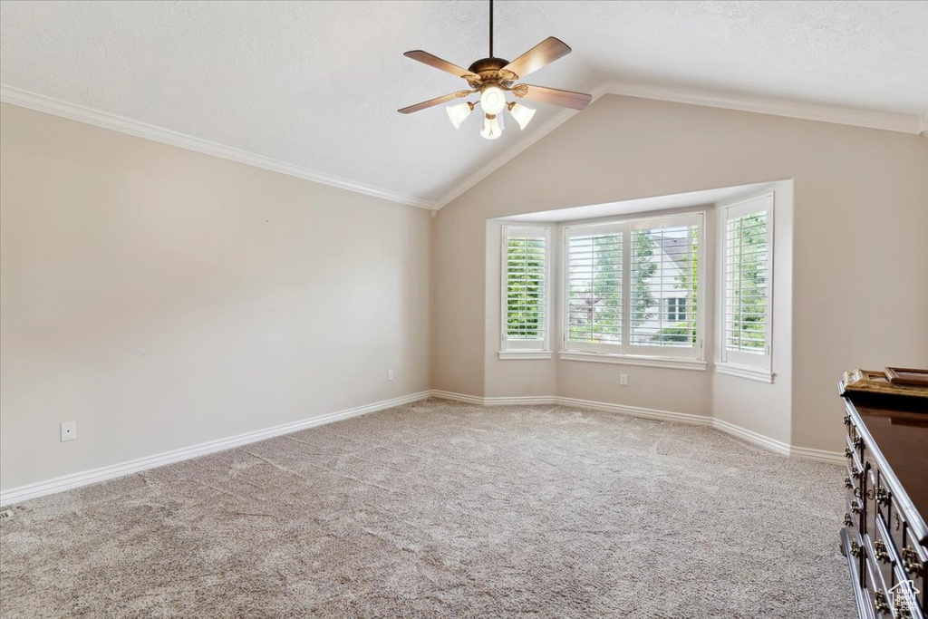 Empty room featuring ceiling fan, vaulted ceiling, light carpet, and baseboards