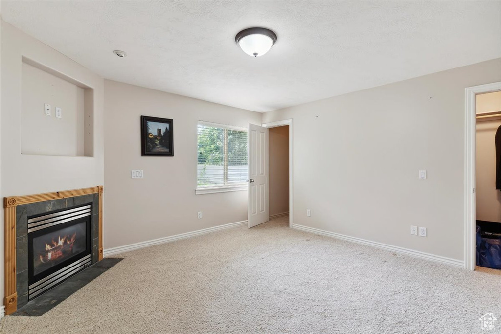 Unfurnished living room with a tiled fireplace, carpet, and baseboards