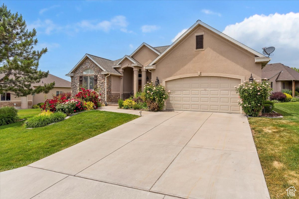 View of front of home with an attached garage, concrete driveway, a front lawn, stone siding, and stucco siding