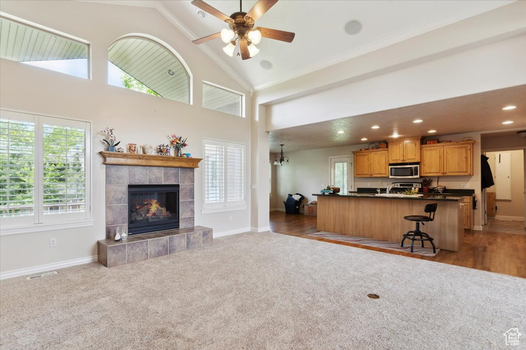 Carpeted living area with baseboards, a tiled fireplace, high vaulted ceiling, a ceiling fan, and recessed lighting