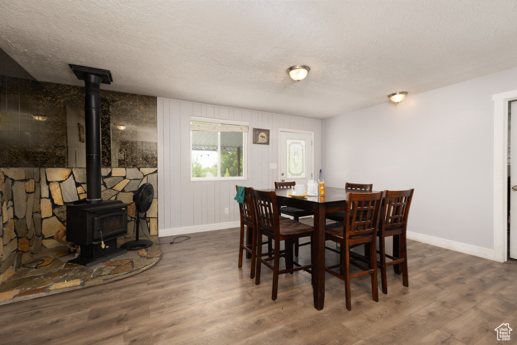 Dining area with a wood stove, a textured ceiling, wood finished floors, and baseboards