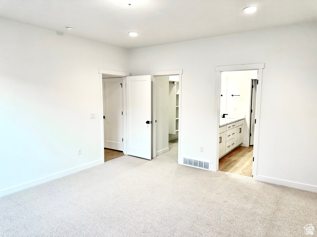 Unfurnished bedroom with light carpet, baseboards, a spacious closet, recessed lighting, and a sink
