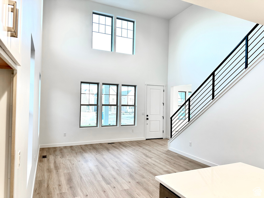 Foyer entrance featuring a high ceiling, light wood-style flooring, stairs, and baseboards