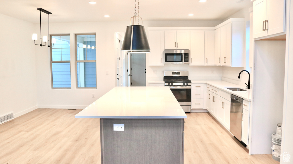 Kitchen featuring stainless steel appliances, a sink, a center island, light wood finished floors, and recessed lighting