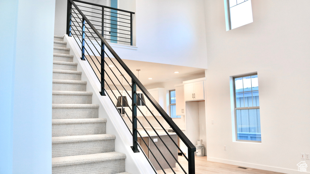 Stairway with plenty of natural light, a high ceiling, wood finished floors, baseboards, and recessed lighting