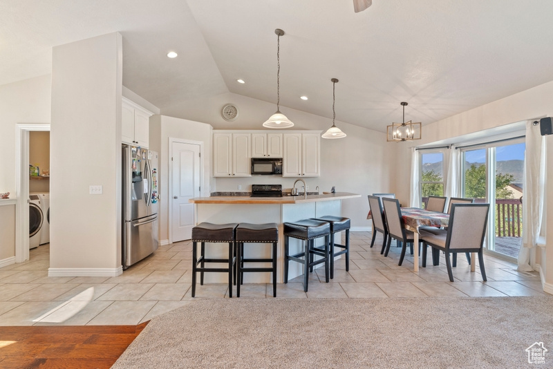 Kitchen with stainless steel fridge, black microwave, washer / dryer, range, and vaulted ceiling
