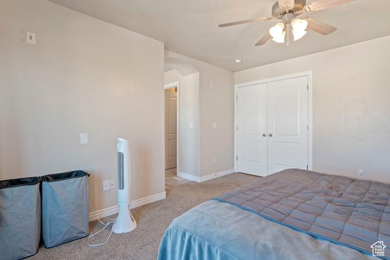 Carpeted bedroom with arched walkways, ceiling fan, baseboards, and a closet