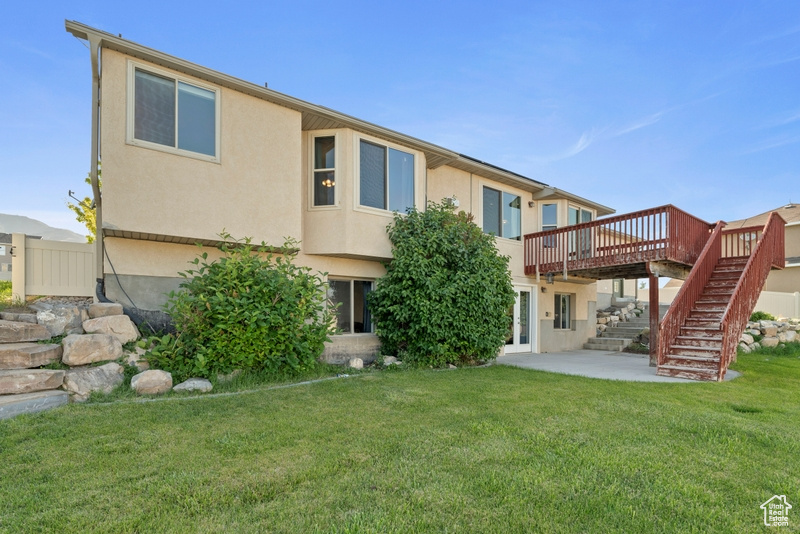 Rear view of property with stairway, a deck, stucco siding, a patio, and a lawn