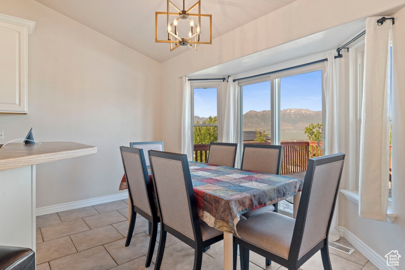 Dining space featuring vaulted ceiling, a mountain view, baseboards, a chandelier, and light tile patterned floors