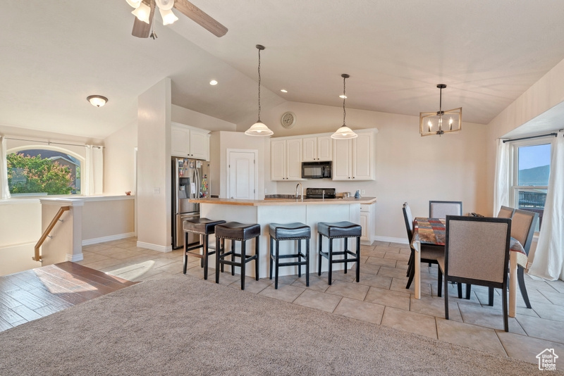 Kitchen with black microwave, stainless steel refrigerator with ice dispenser, white cabinets, a breakfast bar area, and a chandelier