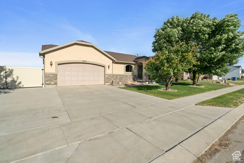 View of front of home featuring stucco siding, a garage, concrete driveway, a front yard, and stone siding