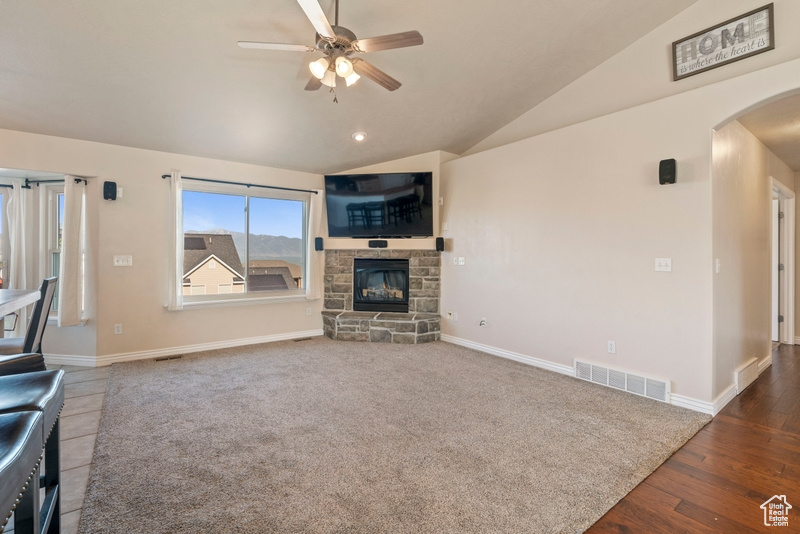 Unfurnished living room with arched walkways, a ceiling fan, vaulted ceiling, baseboards, and a stone fireplace