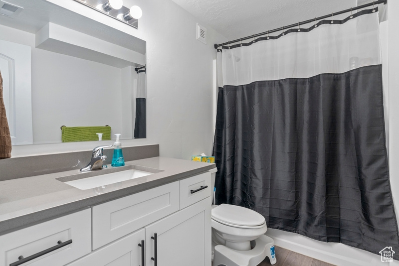 Full bathroom with vanity, toilet, shower / bathtub combination with curtain, wood finished floors, and a textured ceiling