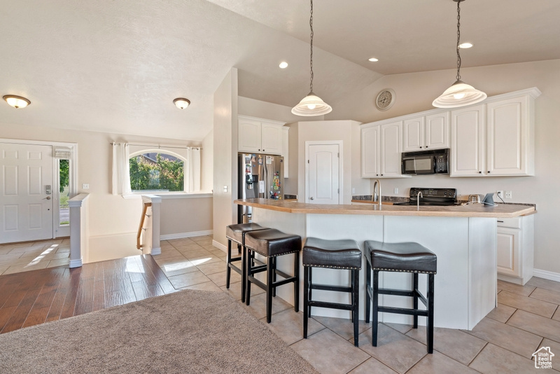 Kitchen featuring black microwave, stainless steel fridge with ice dispenser, vaulted ceiling, baseboards, and a kitchen breakfast bar