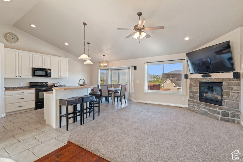 Kitchen with black appliances, lofted ceiling, a ceiling fan, open floor plan, and a kitchen breakfast bar
