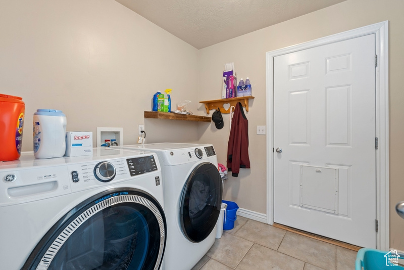 Washroom with washing machine and dryer, light tile patterned floors, and baseboards