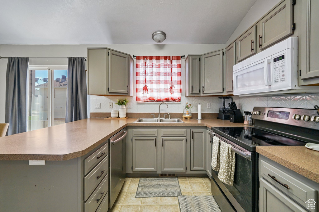 Kitchen with stainless steel appliances, a sink, a peninsula, gray cabinets, and vaulted ceiling