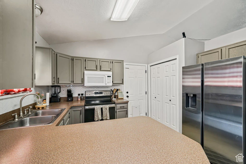 Kitchen with appliances with stainless steel finishes, a sink, lofted ceiling, a peninsula, and backsplash