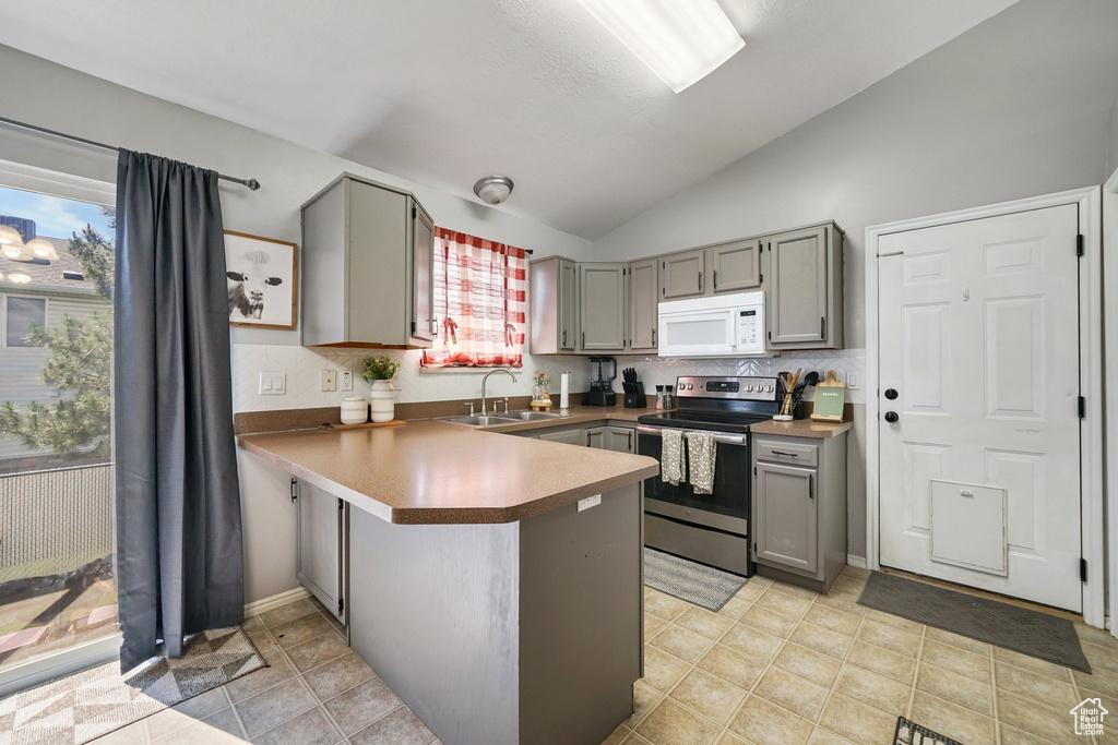 Kitchen featuring white microwave, stainless steel range with electric stovetop, gray cabinets, a sink, and a peninsula