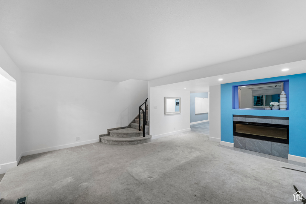 Unfurnished living room featuring stairway, carpet, baseboards, a tile fireplace, and recessed lighting