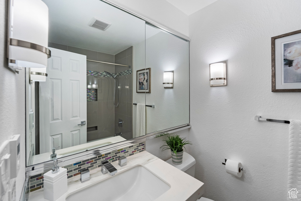 Bathroom with decorative backsplash, toilet, a shower, vanity, and a textured wall