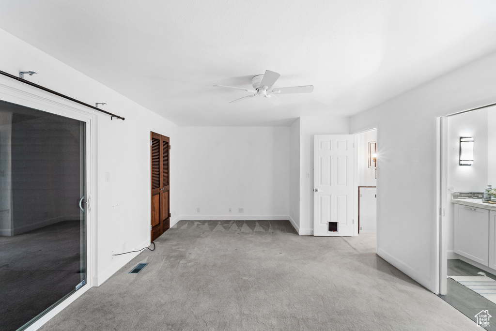 Unfurnished bedroom featuring light colored carpet, baseboards, connected bathroom, and a ceiling fan