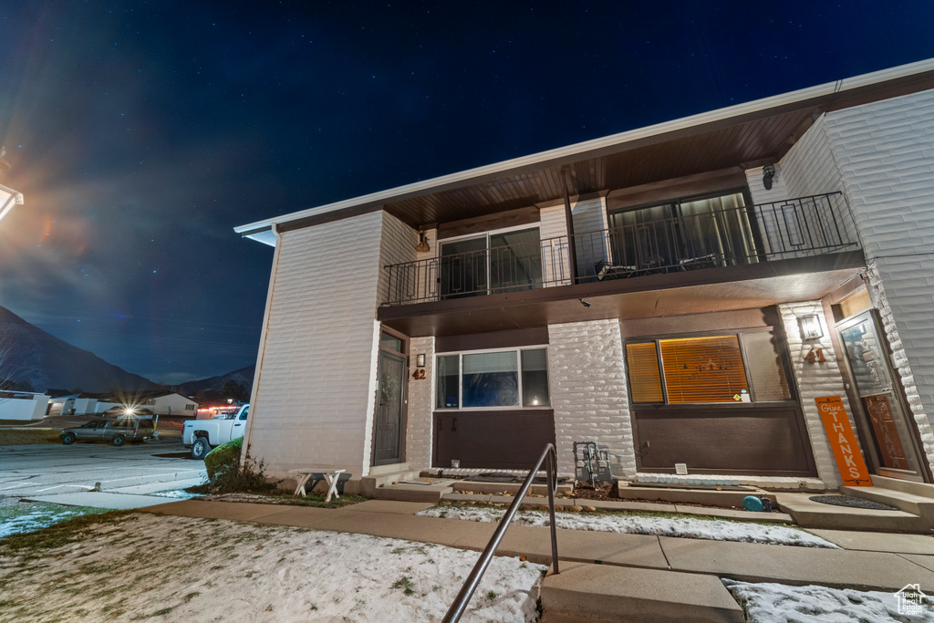 Back of house at twilight with entry steps, a balcony, and brick siding