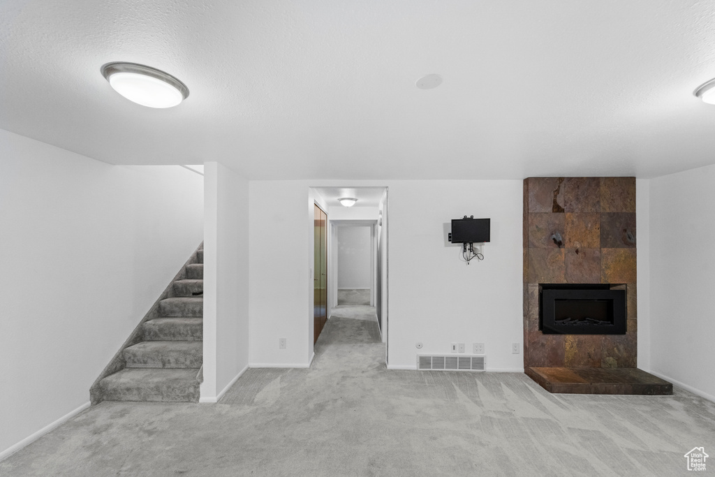 Unfurnished living room with carpet floors, stairs, a tile fireplace, baseboards, and a textured ceiling