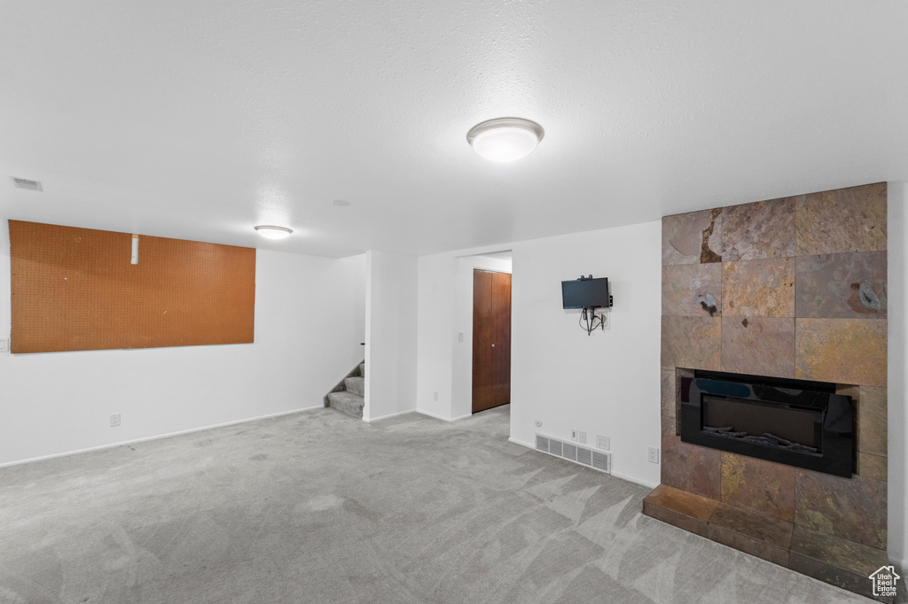 Unfurnished living room featuring stairs, carpet flooring, a tile fireplace, and baseboards