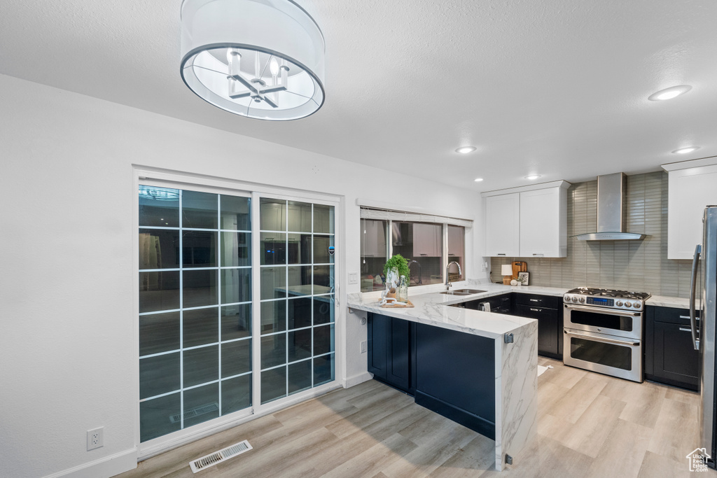 Kitchen featuring wall chimney exhaust hood, range with two ovens, light wood-style flooring, a sink, and recessed lighting