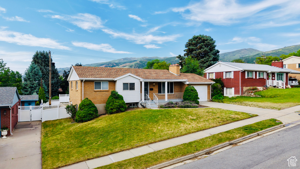 Single story home with a porch, a mountain view, concrete driveway, brick siding, and a gate