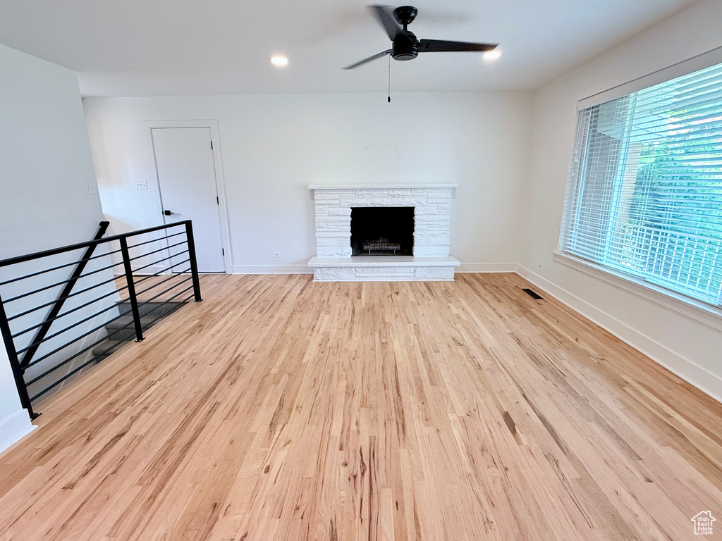 Unfurnished living room featuring a ceiling fan, wood finished floors, a stone fireplace, baseboards, and recessed lighting