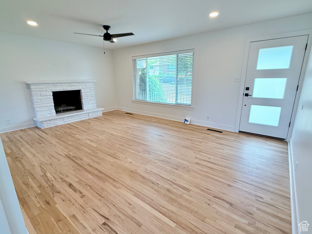 Unfurnished living room featuring wood finished floors, ceiling fan, a stone fireplace, baseboards, and recessed lighting