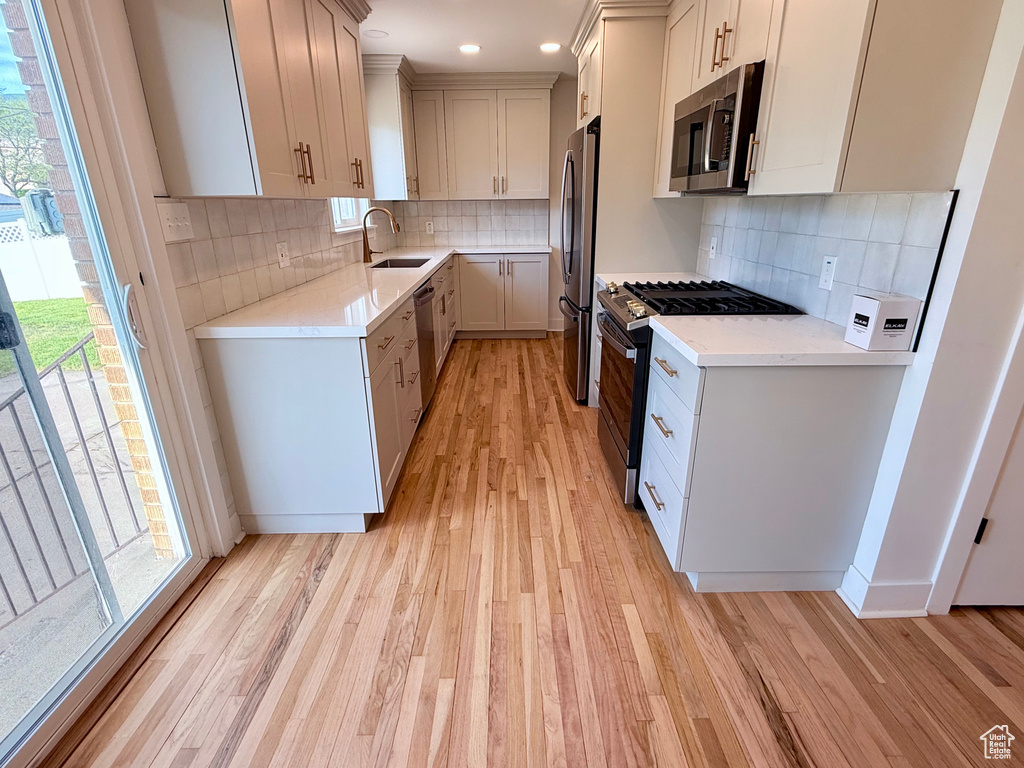 Kitchen featuring stainless steel appliances, a sink, light wood finished floors, decorative backsplash, and recessed lighting