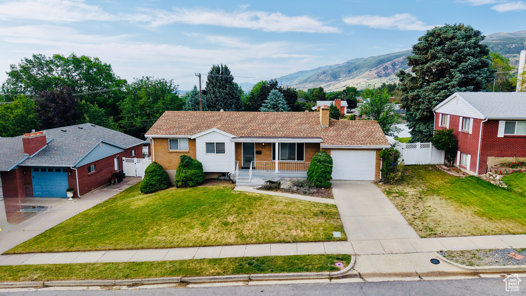 Single story home with covered porch, concrete driveway, a garage, a mountain view, and a chimney
