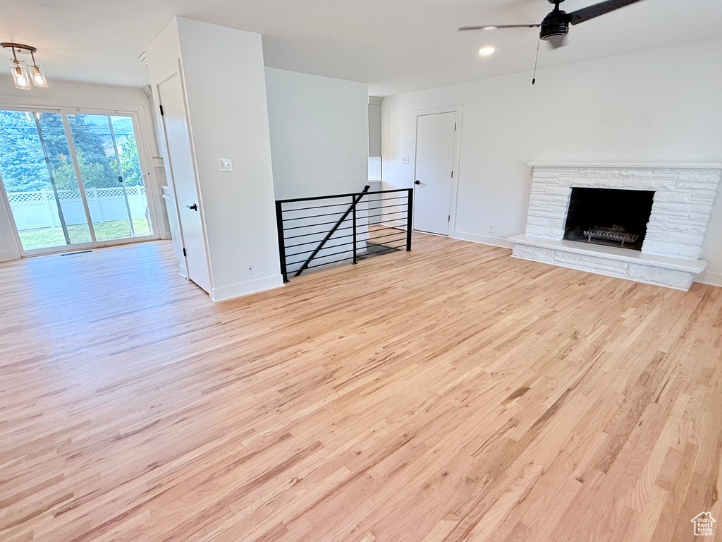 Unfurnished living room with wood finished floors, ceiling fan, baseboards, and a stone fireplace