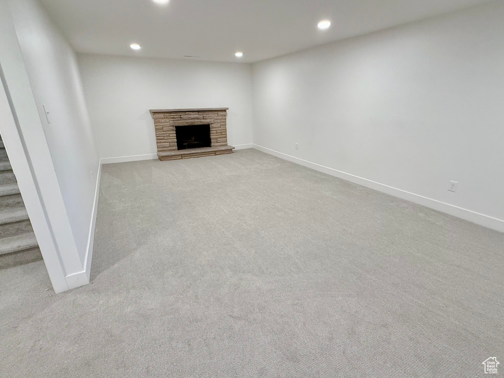Unfurnished living room featuring recessed lighting, light colored carpet, baseboards, a stone fireplace, and stairs