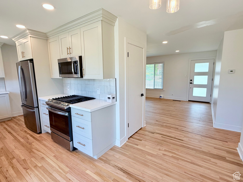 Kitchen with appliances with stainless steel finishes, light wood finished floors, light countertops, tasteful backsplash, and baseboards