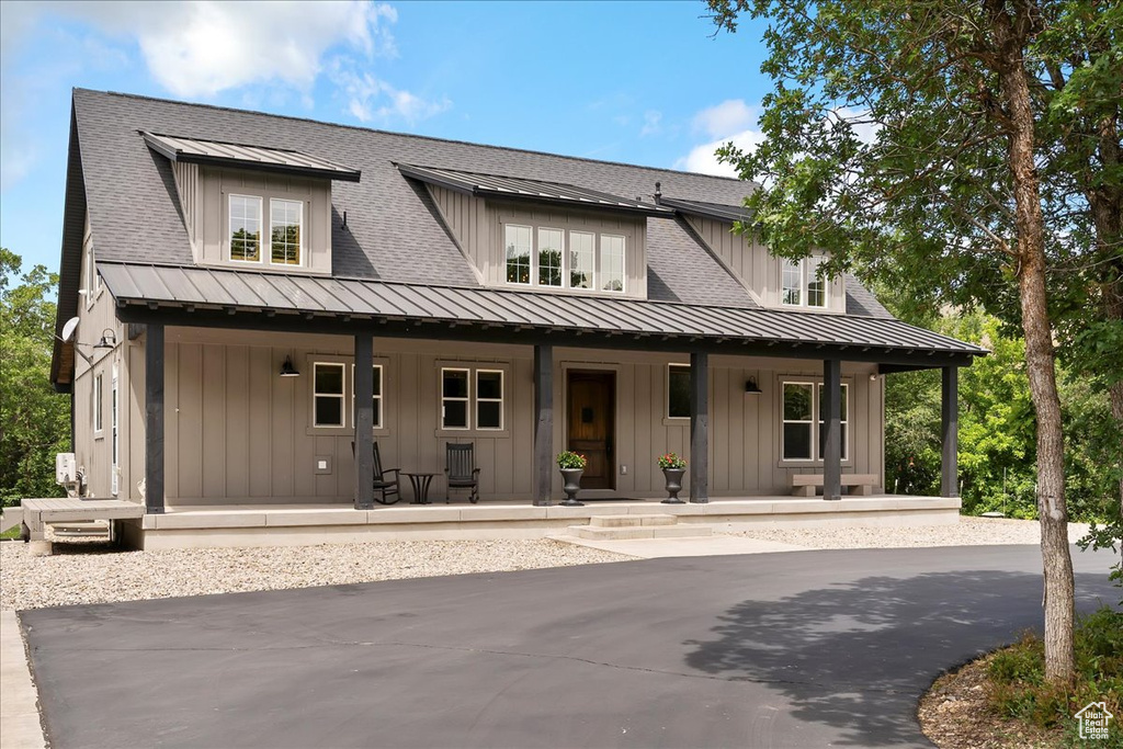 View of front facade with covered porch, a standing seam roof, board and batten siding, roof with shingles, and metal roof