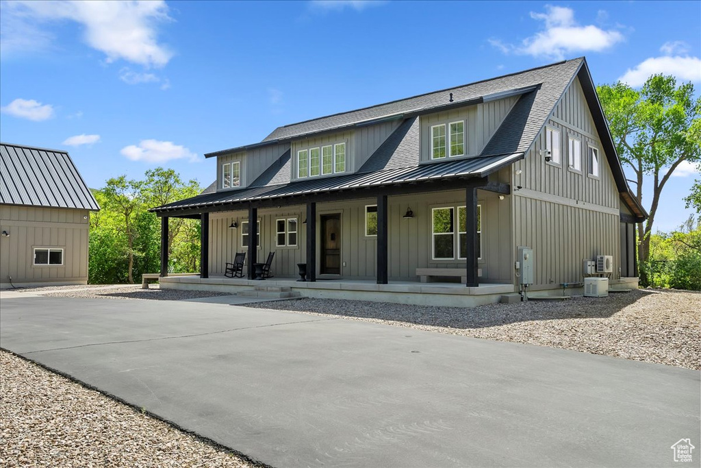 Modern inspired farmhouse with a porch, metal roof, board and batten siding, a standing seam roof, and central air condition unit
