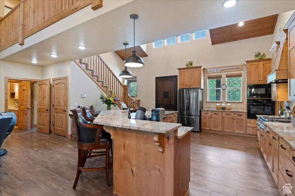 Kitchen with black appliances, a breakfast bar area, dark wood-type flooring, a center island, and light stone countertops