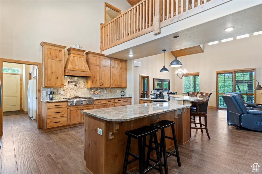 Kitchen with a towering ceiling, custom range hood, freestanding refrigerator, stainless steel gas cooktop, and dark wood finished floors