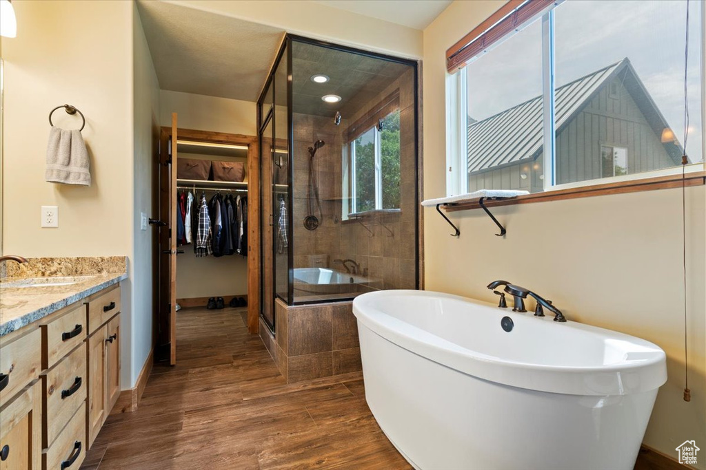 Bathroom with a stall shower, a freestanding bath, a spacious closet, vanity, and wood finished floors