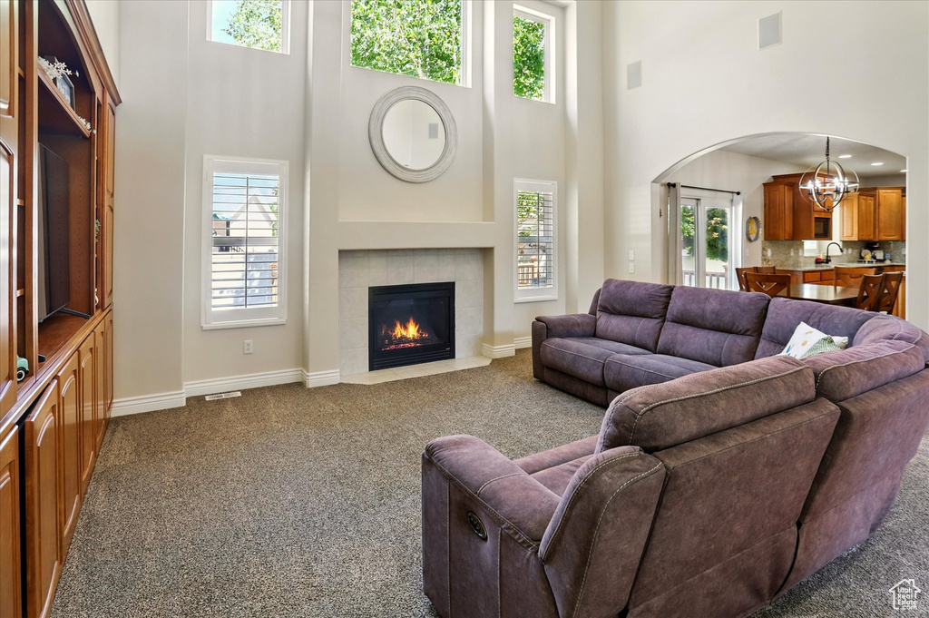Living room featuring a high ceiling, dark colored carpet, arched walkways, a chandelier, and baseboards