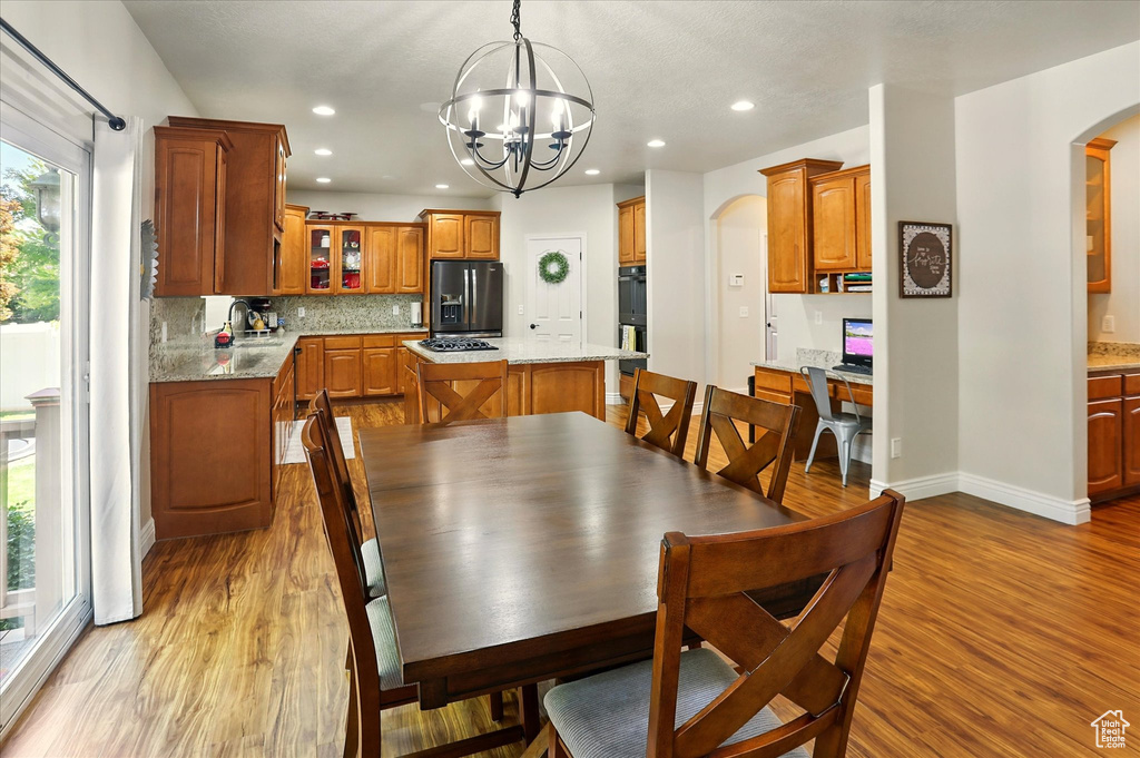Dining space featuring arched walkways, light wood finished floors, a chandelier, baseboards, and recessed lighting