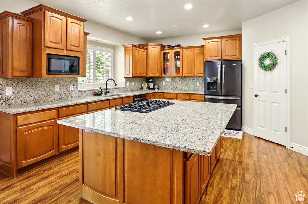 Kitchen with refrigerator with ice dispenser, black microwave, wood finished floors, light stone counters, and recessed lighting