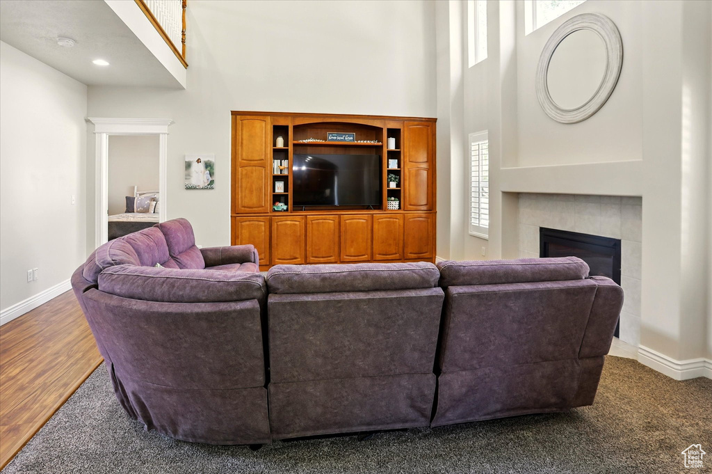 Living room featuring a high ceiling, baseboards, a tiled fireplace, and wood finished floors